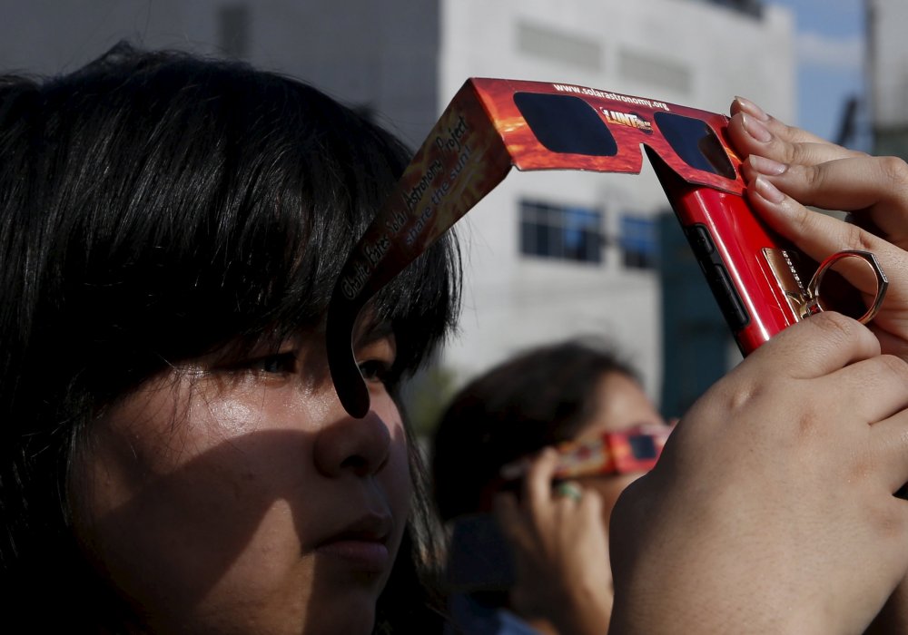 Член Астрономической Лиги Филиппин использует солнечные очки, чтобы сфотографировать частичное солнечное затмение на мобильный телефон. © REUTERS