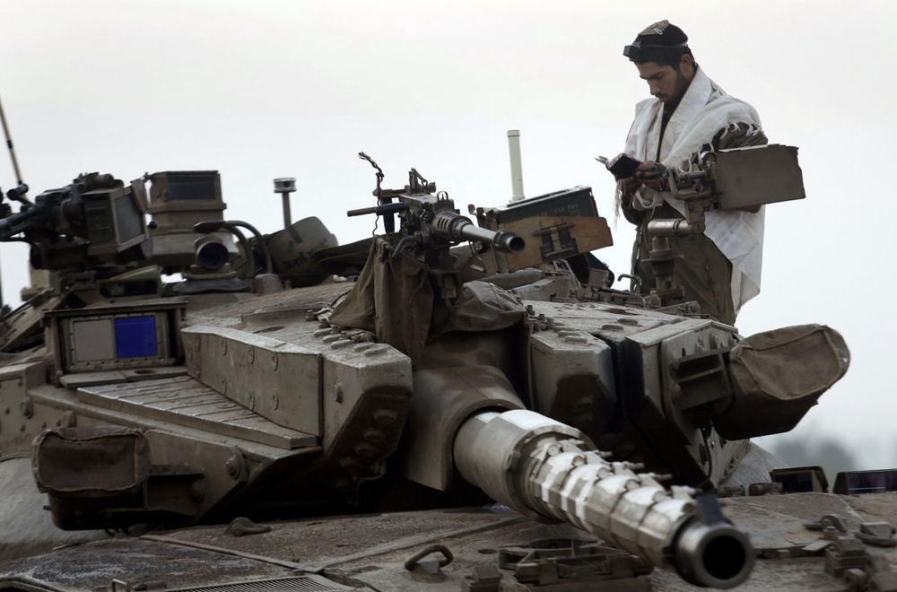 Израильский солдат читает молитву, стоя на танке на границе сектора Газа. Фото REUTERS/Yannis Behrakis©