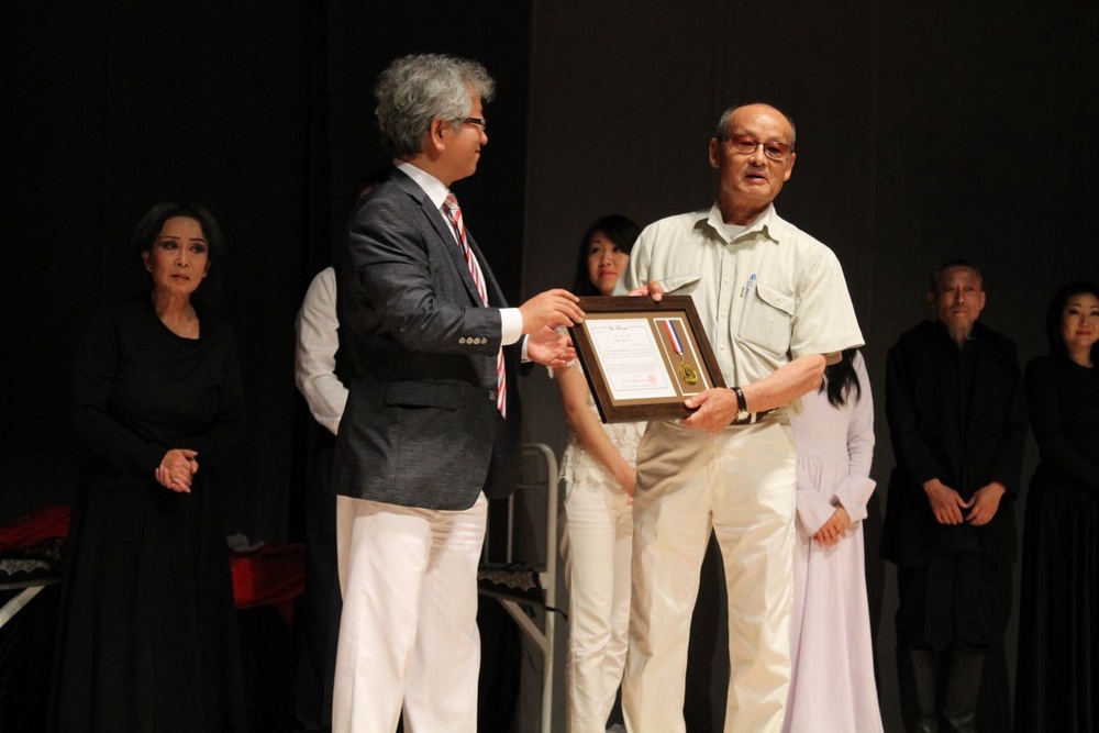 Председатель Союза театральных деятелей Республики Корея Юн Бон Гу вручает специальную грамоту заведующему литературной частью Корейского театра Цой Ен Гыну 