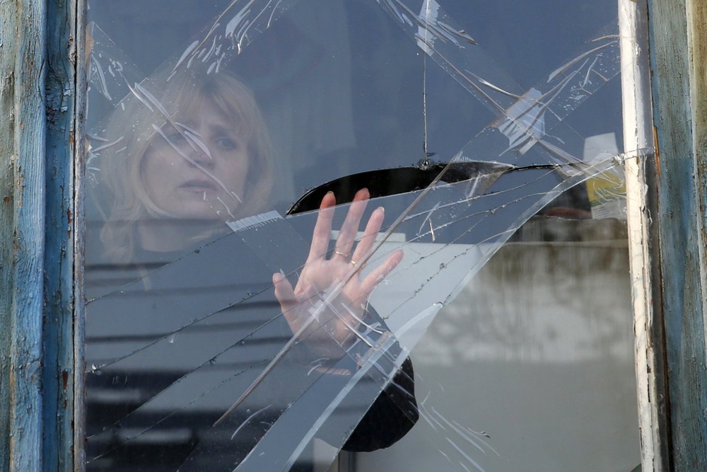 Жительница Донецка осматривает разбитое в результате обстрела окно, 14 февраля 2015 года. Фото ©Reuters 