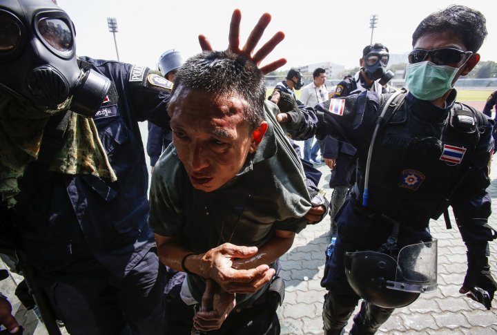 Полицейские эскортируют протестующего во время столкновений на стадионе в Бангкоке. ©REUTERS