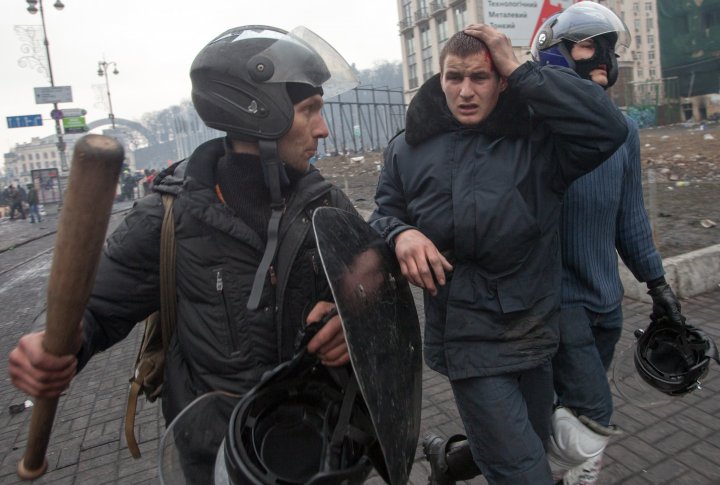 Антиправительственные протестующие задерживают раненого милиционера во время столкновений на майдане Независимости в Киеве 20 февраля 2014. ©REUTERS