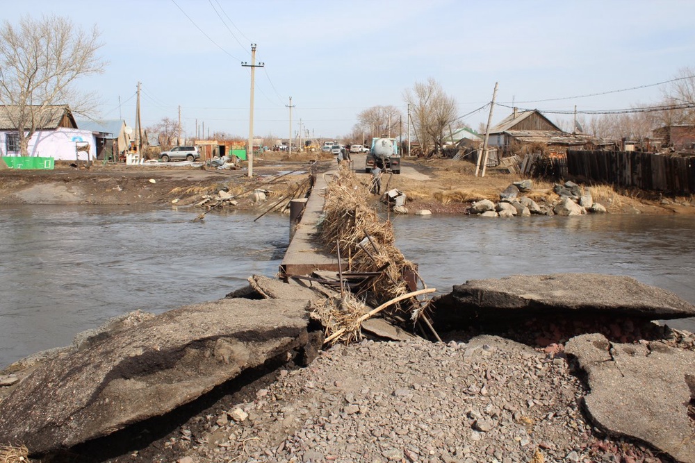 Русло реки Кокпекты, протекающей через затопленный поселок и пешеходный мост.