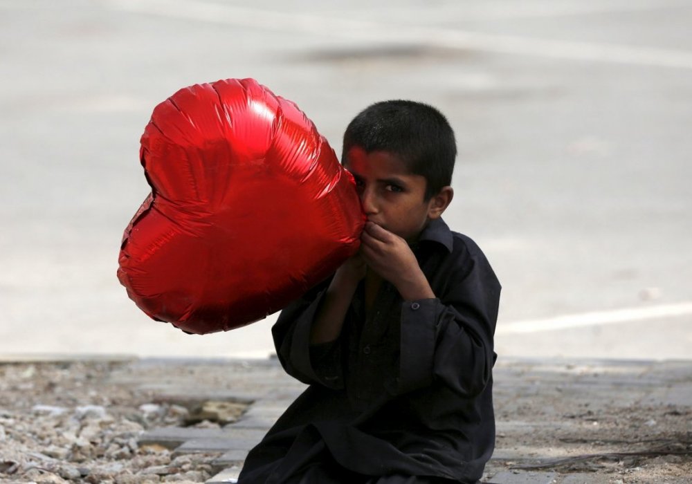 Мальчик надувает шарик в форме сердца для продажи. Карачи, Пакистан. ©REUTERS/Akhtar Soomro