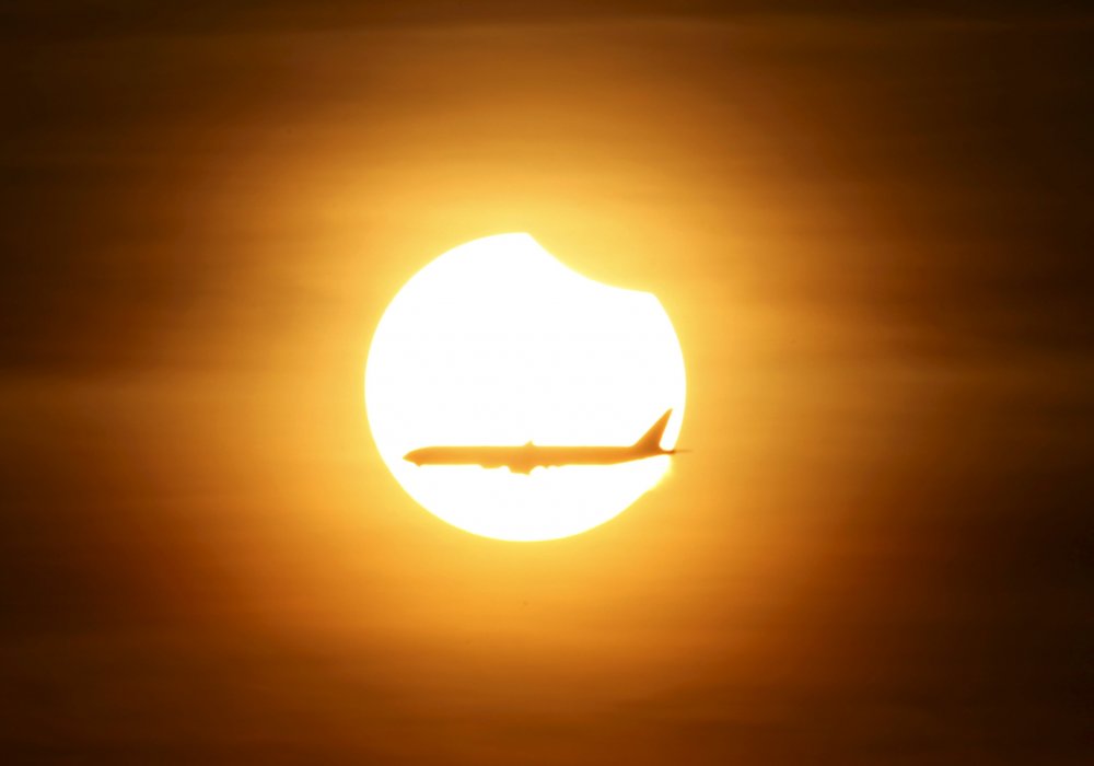 Самолет летит на фоне солнца в тот момент, когда наступает частичное солнечное затмение. Сингапур. © REUTERS