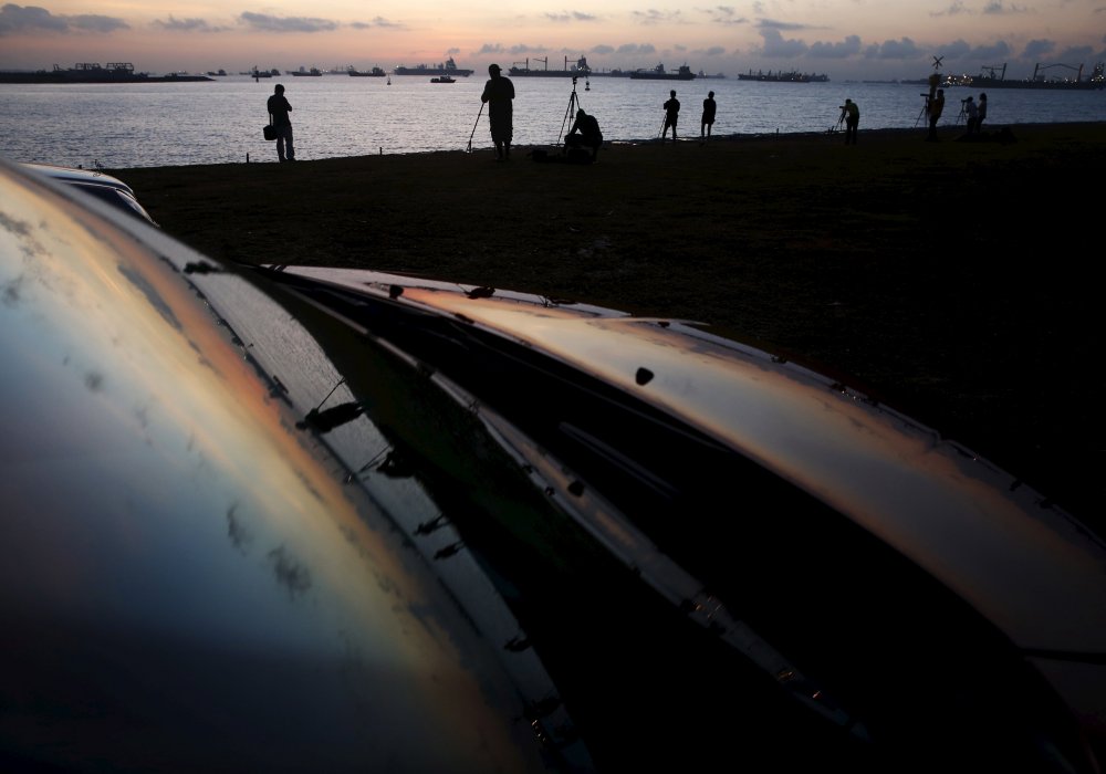 Люди готовятся сфотографировать частичное солнечное затмение во время восхода солнца среди грузовых судов в Сингапуре. © REUTERS