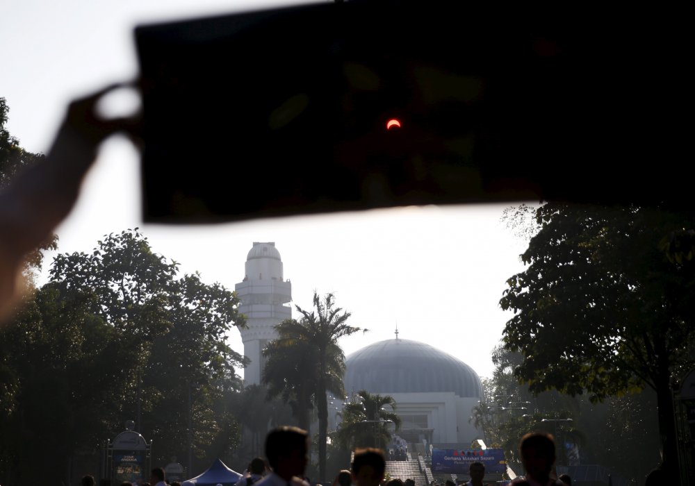 Студент наблюдает частичное солнечное затмение через фильтровальную бумагу. Планетарий в Куала-Лумпуре, Малайзия. © REUTERS