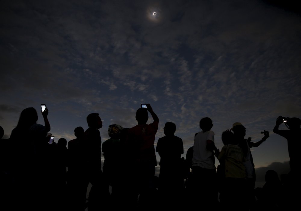 Люди смотрят и фотографируют солнечное затмение на пляже. Индонезия. © REUTERS
