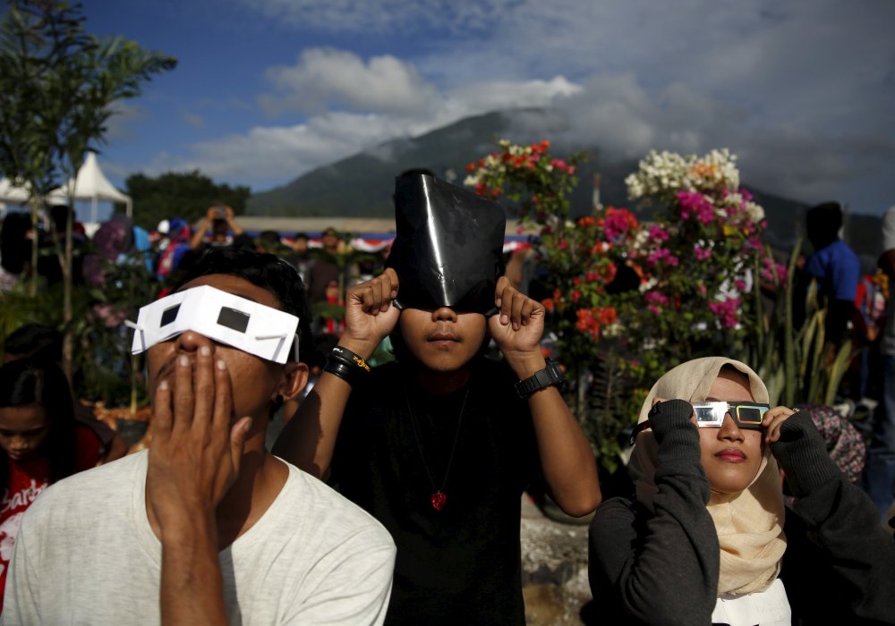 Молодые люди смотрят солнечное затмение через самодельные солнечные фильтры. Индонезия. © REUTERS