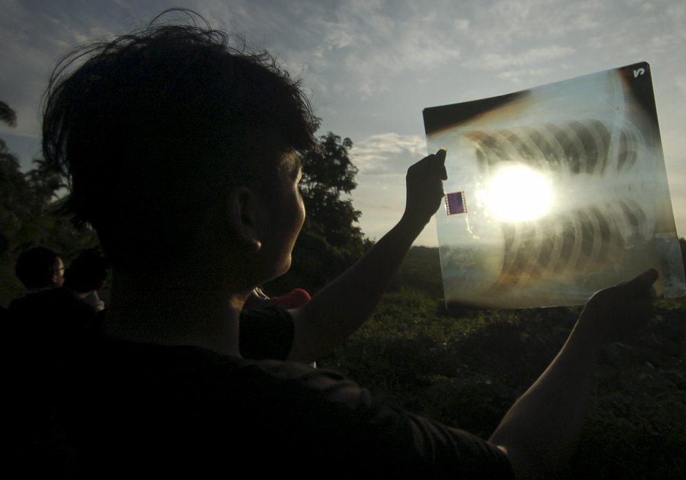 Человек использует медицинскую рентгеновскую пленку, чтобы увидеть солнечное затмение. Провинция Западная Суматра, Индонезия. © REUTERS
