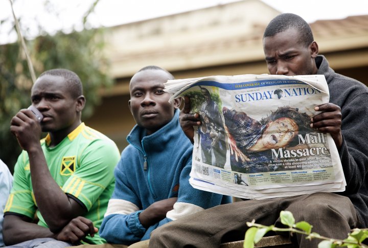 Человек читает ежедневную газету на краю периметра безопасности у торгового центра Вестгейт в Найроби, где боевики держат заложников,  22 сентября 2013 г. Фото ©REUTERS