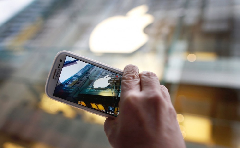 Прохожий фотографирует логотип Apple Store c помощью смартфона Samsung Galaxy. Фото ©REUTERS