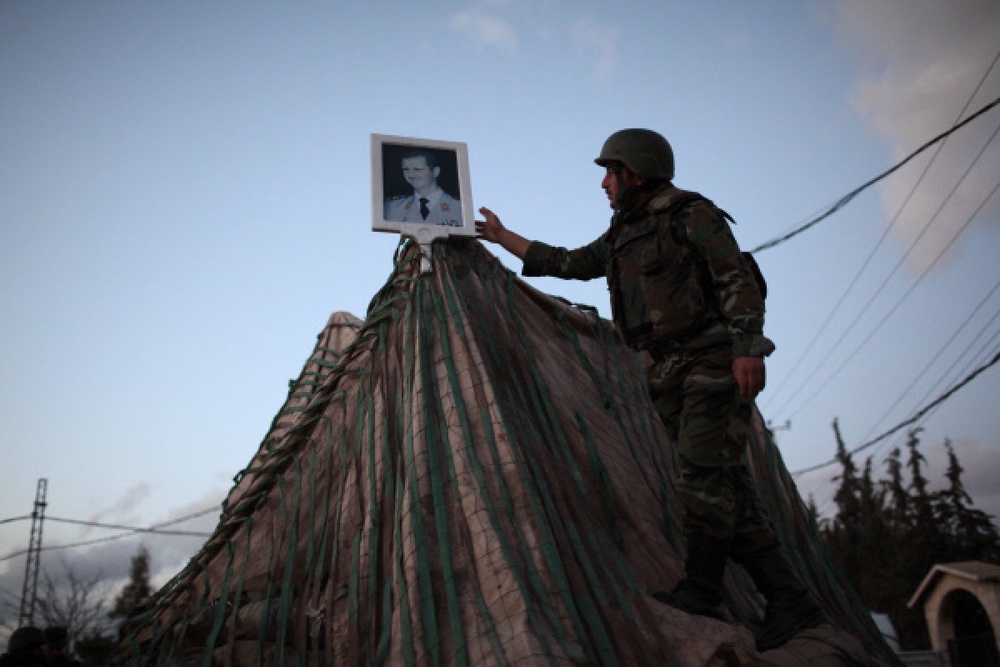 Военнослужащий сирийской армии устанавливает портрет президента Башара Асада на блокпосту. Фото ©РИА Новости