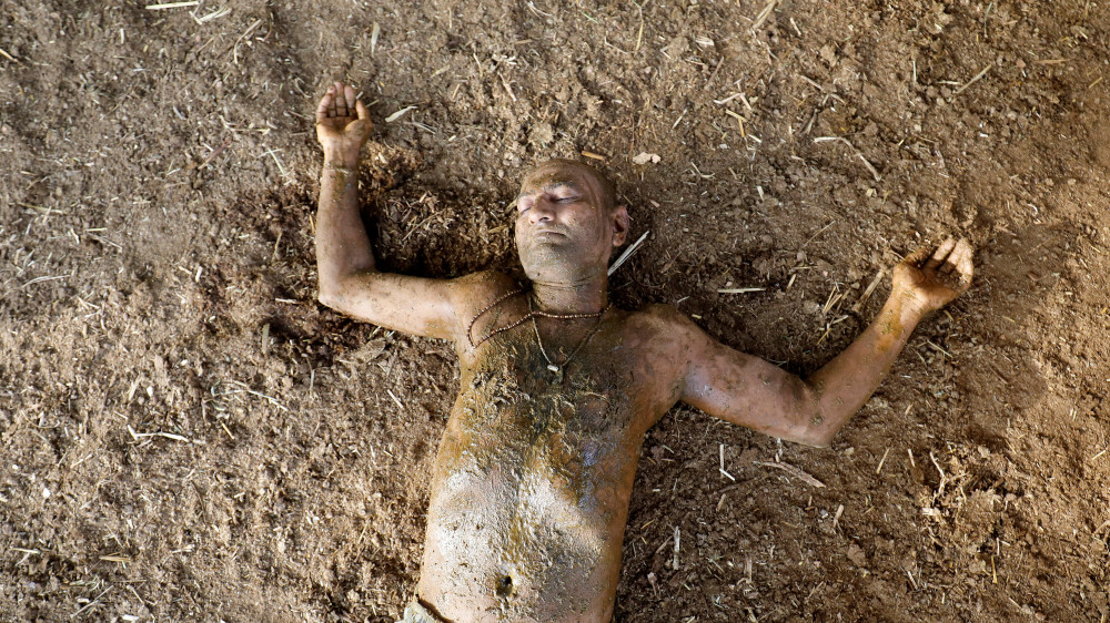 Мужчина лежит на земле, обмазавшись коровьим навозом, который используется в Индии, как лекарство от коронавируса. © Reuters